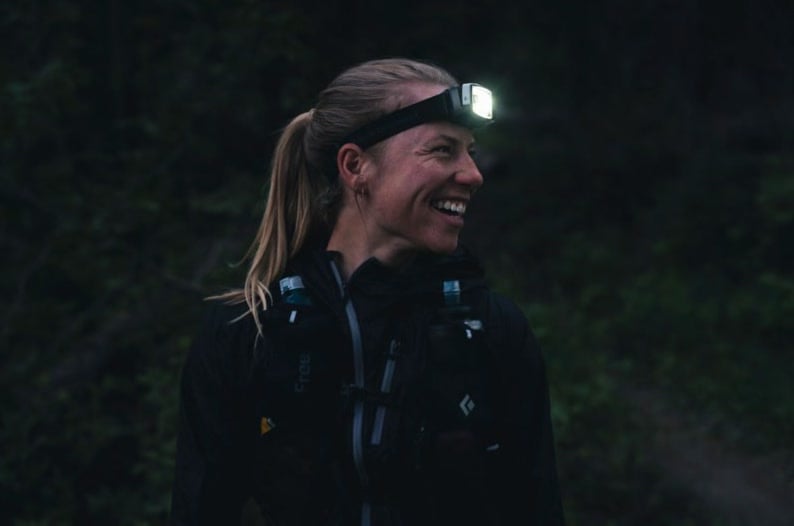A climber smiling in the dark under a headlamp