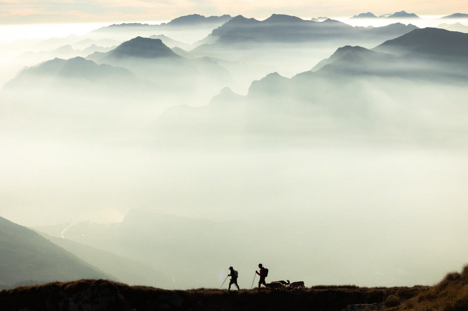 Two small figures walking a ridge above valleys filled with morning mist