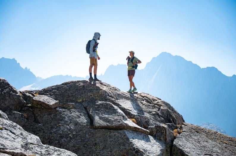 Two hikers on a rocky summit above alpine valleys
