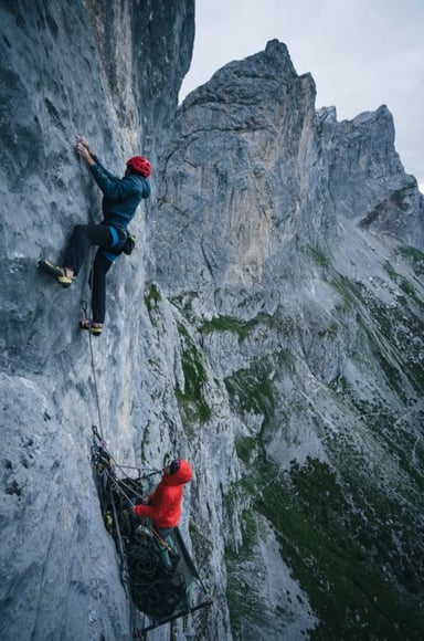 A climber and belayer on a steep grey rock face